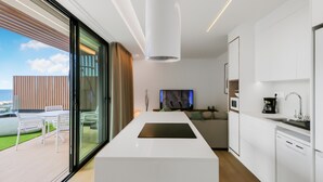 A modern kitchen with a central island, a dining area with a glass wall, and a living area with a TV. - Paraisos de Agaete Penthouse Views (El Turman)