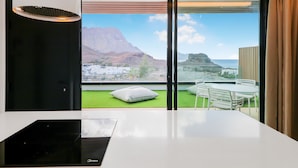 A modern room with a large window offering a view of a mountainous landscape and a coastal area. - Paraisos de Agaete Penthouse Views (El Turman)