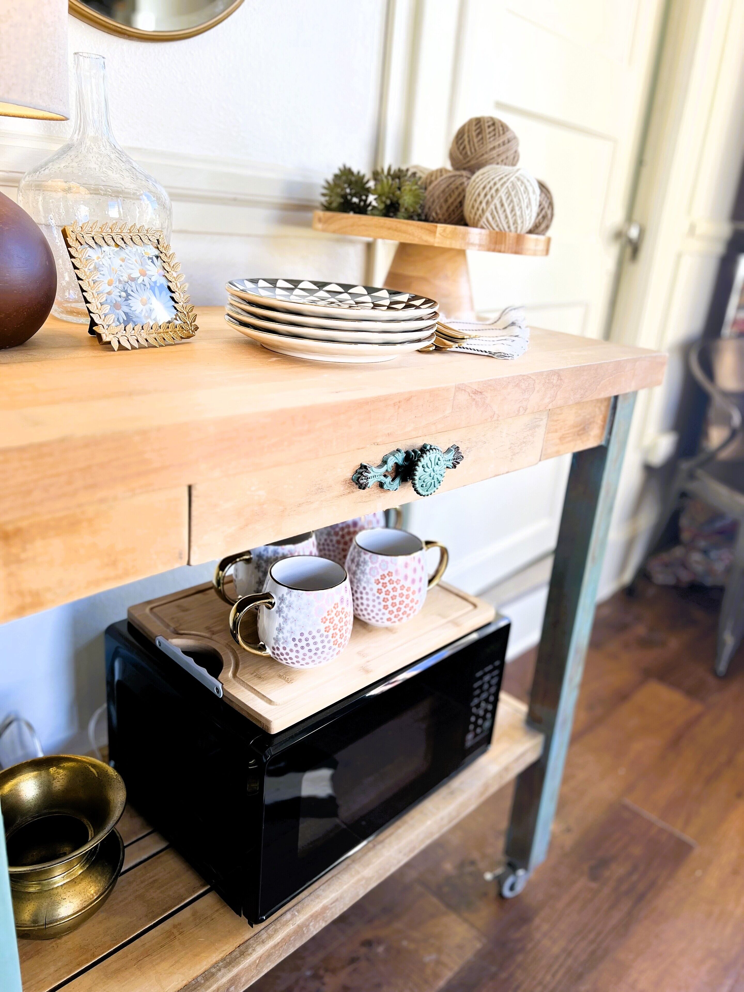 A kitchen counter with a microwave, a stack of plates, a decorative glass bottle, and a framed picture.