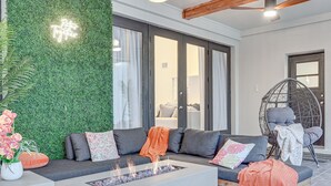 A modern living room with a grey sofa, a glass-top coffee table with a fire feature, a green wall with a neon sign, and a large window with curtains. - Valrico Villa: Pool, Spa, Court & Game Room (Valrico)