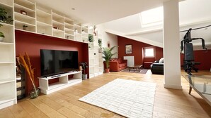 Un salon moderne doté d’un téléviseur à écran plat, de planchers en bois et d’un mur d’accent rouge.