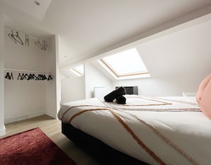 A bedroom with a skylight, a bed with a patterned bedspread, and a red rug.