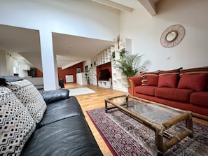 A spacious living area with a black leather sofa, a red sofa, and a glass coffee table. There is a patterned rug on the floor, and a potted plant is visible.