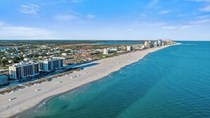 Een kuststreeed met een lang zandstrand, een heldere blauwe oceaan en een rij hoge hotels langs de kust.
