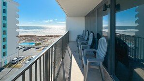 Een balkon met uitzicht op de oceaan, een zwembad en verschillende stoelen.