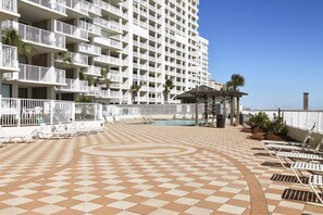 A hotel with multiple balconies, a pool area with lounge chairs, and a view of the ocean.