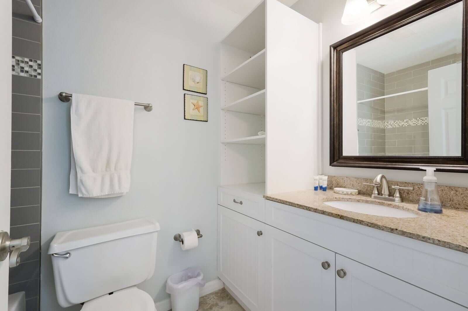 A bathroom with a toilet, sink, and mirror. There are two framed pictures on the wall and a towel hanging on the wall.