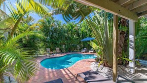 Une piscine entourée de palmiers et de chaises longues, avec une terrasse en briques.