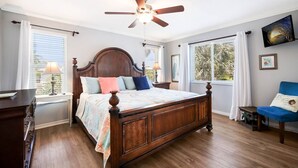 Une chambre avec un lit en bois, un ventilateur de plafond, une fenêtre avec des stores et une chaise.