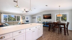 Une cuisine spacieuse avec un grand îlot central, une table à manger en bois et des ventilateurs de plafond.