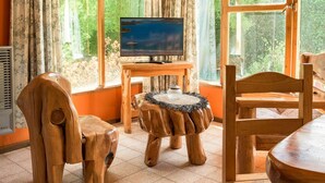 Una habitación acogedora con muebles de madera, ventanas amplias y un televisor sobre un mueble de madera.