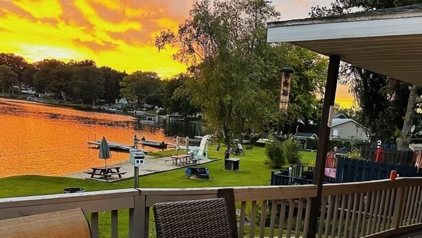 Une terrasse agrémentée d’un foyer extérieur, de sièges et offrant une vue sur un lac au coucher du soleil.