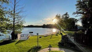 Une propriété paisible située au bord d’un lac, avec une pelouse verdoyante, une jetée en bois et un sentier menant à une autre jetée.