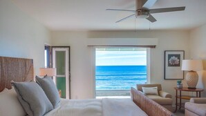 Habitación de hotel con cama, ventilador de techo, vista al océano, una silla y una lámpara.