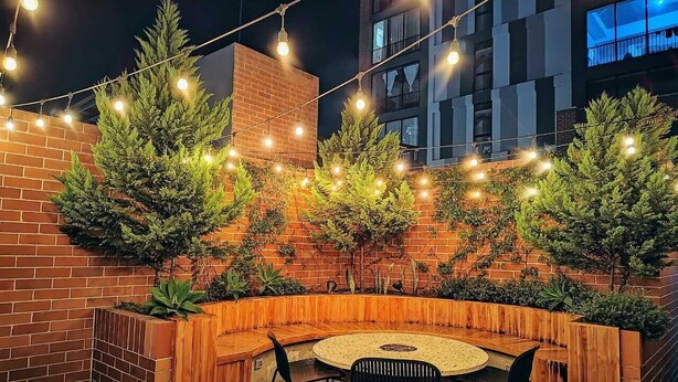 An outdoor seating area with a round table and chairs, surrounded by a brick wall and wooden planters with greenery. - Jacuzzi Getaway, in the Heart of Zone 4 (Ciudad de Guatemala)