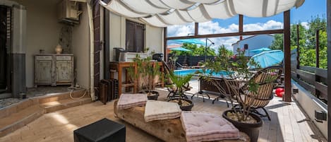 A sunlit patio with a pool, outdoor seating, and potted plants.
