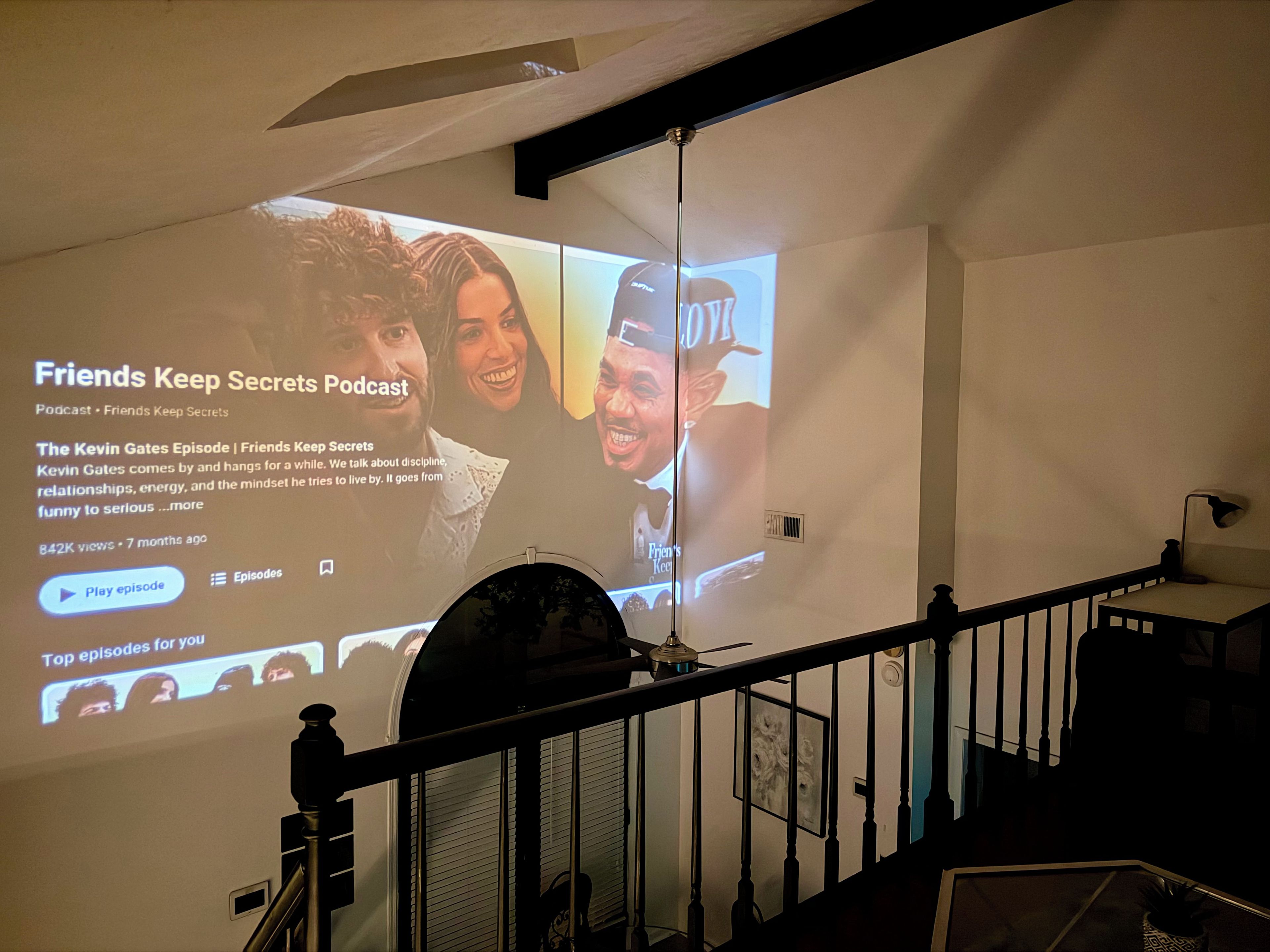 Un écran de projection affiche un épisode de podcast intitulé « L’épisode Kevin Gates », tiré du podcast « Friends Keep Secrets ».