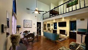 Un vaste espace de vie doté d’un haut plafond, d’un ventilateur de plafond, d’une table à manger avec des chaises, d’un canapé bleu et d’une cheminée.