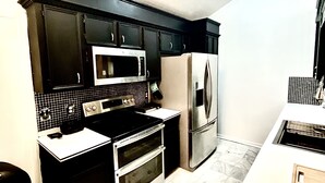 Eine moderne Küche mit schwarzen Schränken, einem Edelstahl-Kühlschrank, einer Mikrowelle und einem Backofen.