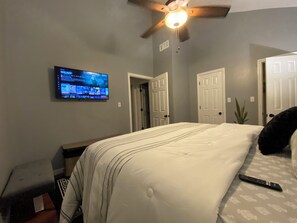 Ein Schlafzimmer mit einem Bett, einem Deckenventilator, einem an der Wand montierten Fernseher und einer Tür.