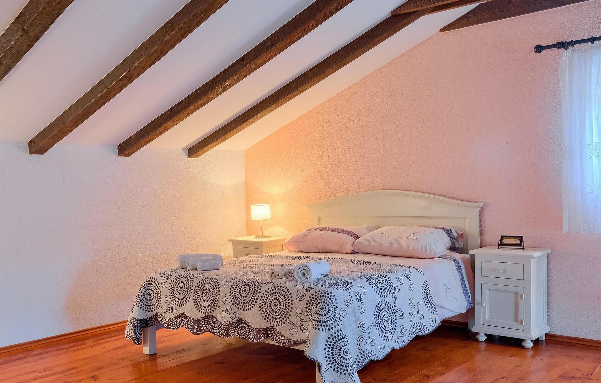 Ein Schlafzimmer mit Holzbalkendecke, einem Bett mit weißem Kopfteil, einem Nachttisch und einem Beistelltisch.