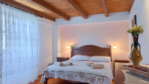 A bedroom with a wooden headboard, two bedside lamps, a bed with rolled towels, a vase with flowers, and a wooden nightstand. - Beach front home in Pula (Pula)