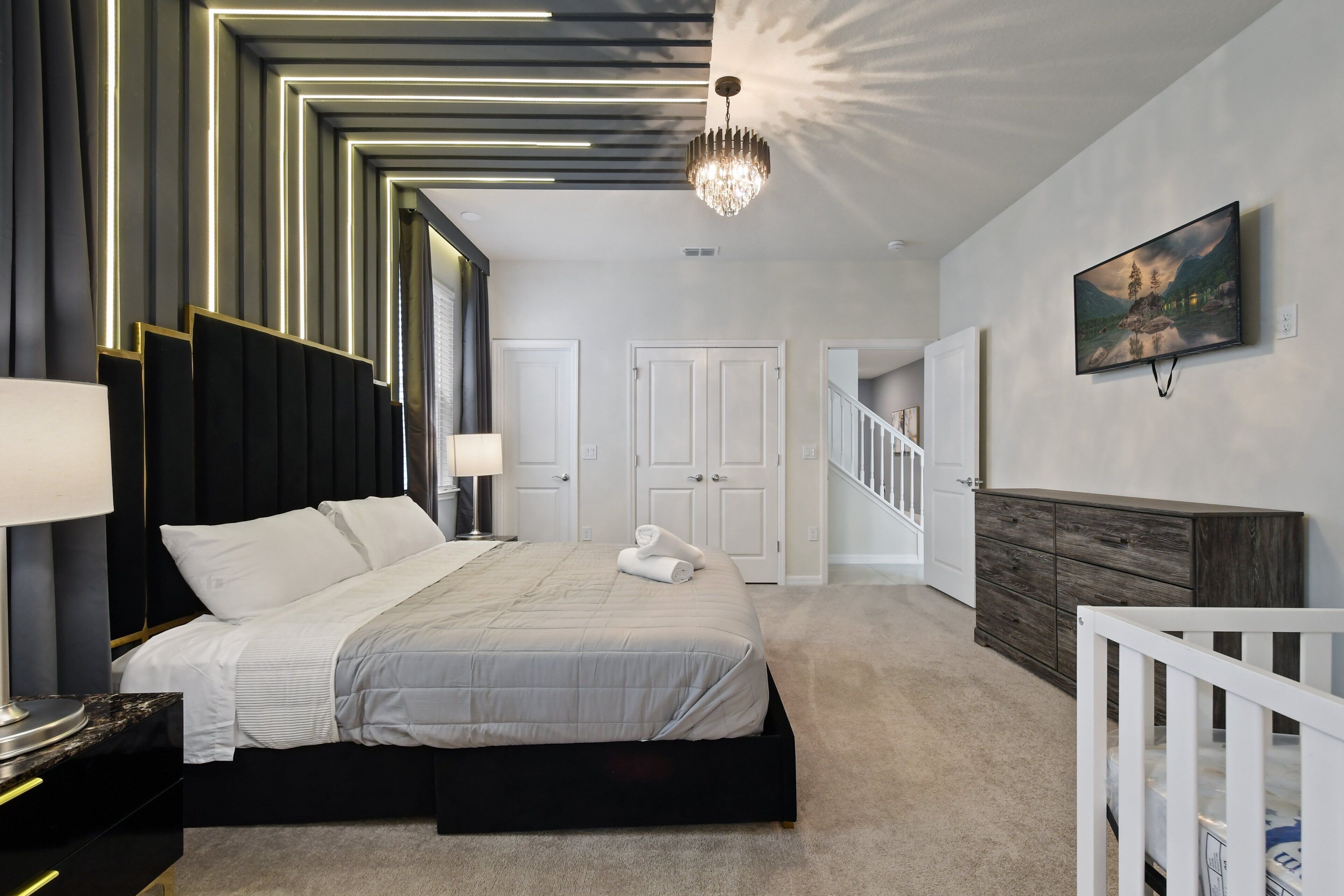 Ein modernes Schlafzimmer mit einem großen Bett, Nachttischlampen, einem Kronleuchter, einem Gemälde und einer Treppe.