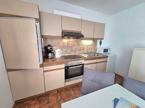 Eine kompakte Küche mit Kühlschrank, Kaffeemaschine, Mikrowelle, Herd und Spüle.