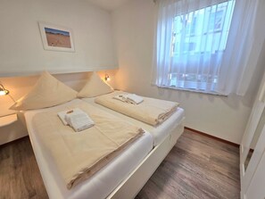 Ein Hotelzimmer mit zwei Betten, einem Nachttisch, einem Wandbild und einem Fenster mit Jalousien.