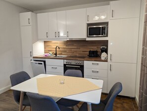 Une cuisine moderne avec des meubles blancs, un four à micro-ondes, une machine à café et une table à manger avec des chaises.