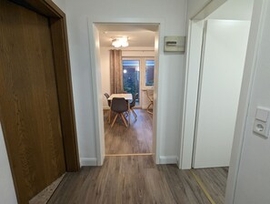 Ein Flur, der zu einem Essbereich mit Tisch und Stühlen führt, mit einem Fenster mit Vorhängen und einem Schild an der Wand.