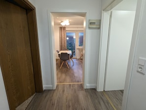 A hallway leading to a dining area with a table and chairs, a window with curtains, and a sign on the wall.