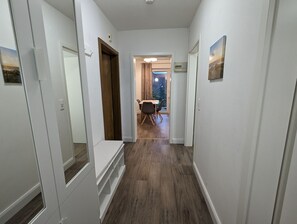 Ein schmaler Korridor mit weißen Wänden und Holzboden, der zu einem Essbereich mit Tisch und Stühlen führt.