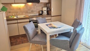 Cocina compacta con estufa, lavamanos y comedor con dos sillas y una mesa.