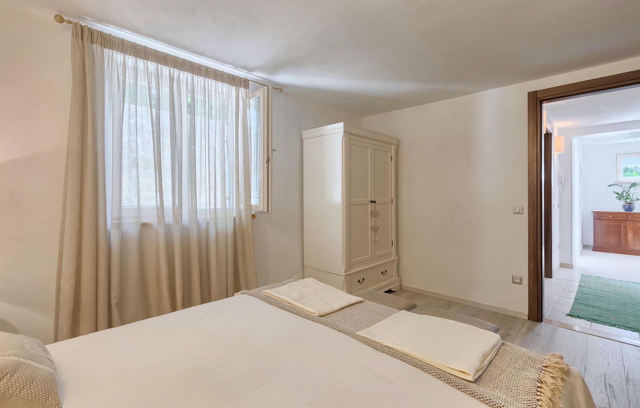 A bedroom with a bed, a wardrobe, and a view of the outside.