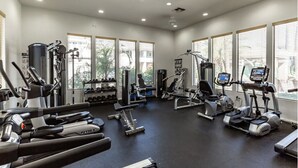 Un gimnasio bien iluminado con diversos equipos de ejercicio, ventanas amplias y un diseño moderno y limpio.