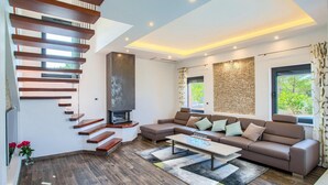 A modern living room with a staircase, a fireplace, a sectional sofa, and a large window.