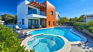 A modern two-story house with a swimming pool, outdoor seating, and lush greenery.