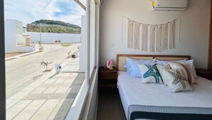 A hotel room with a bed, a nightstand, a wall-mounted air conditioner, and a view of the outside.