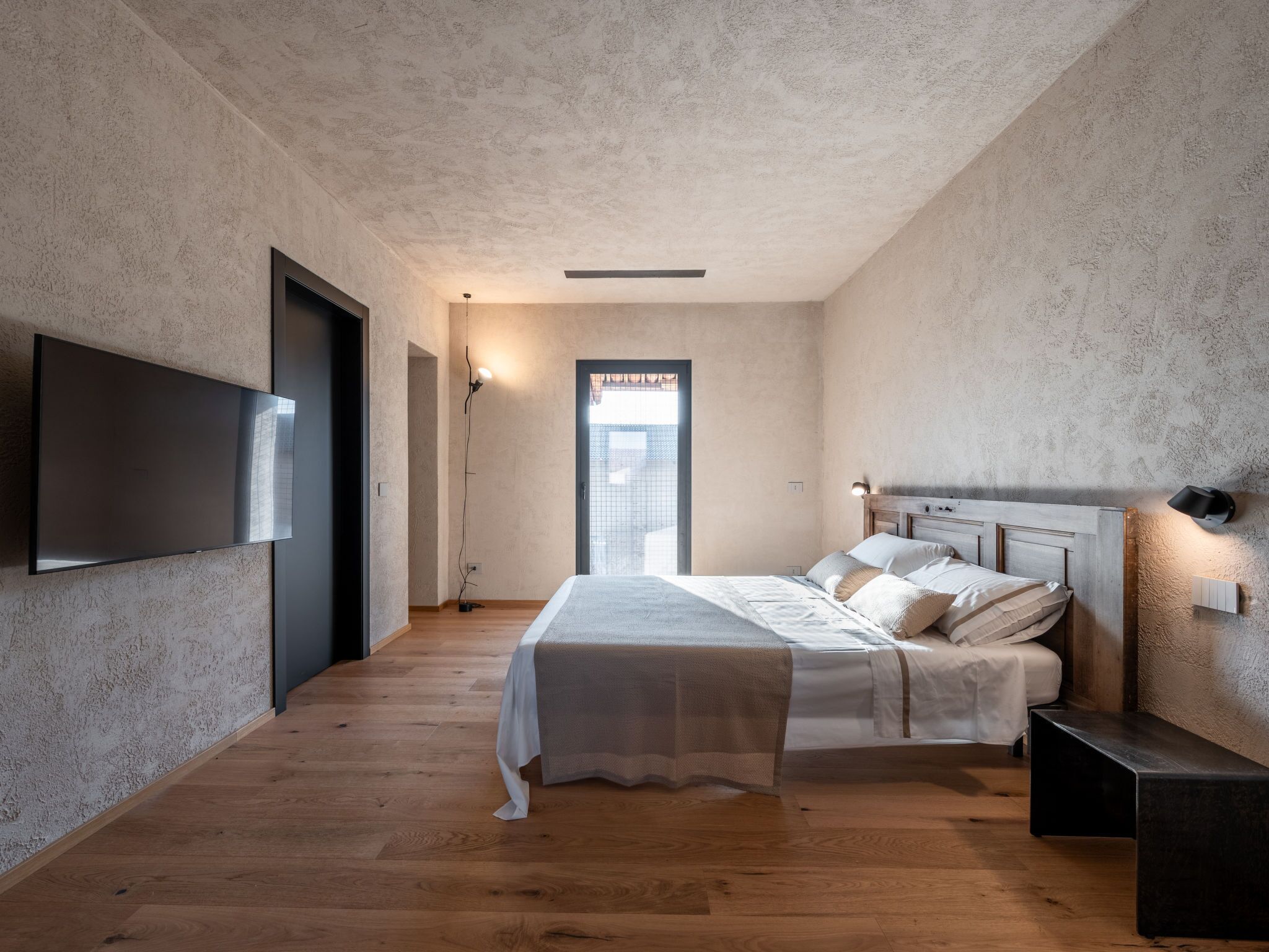 A bedroom with a bed, a TV, a bedside lamp, and a view through a door.