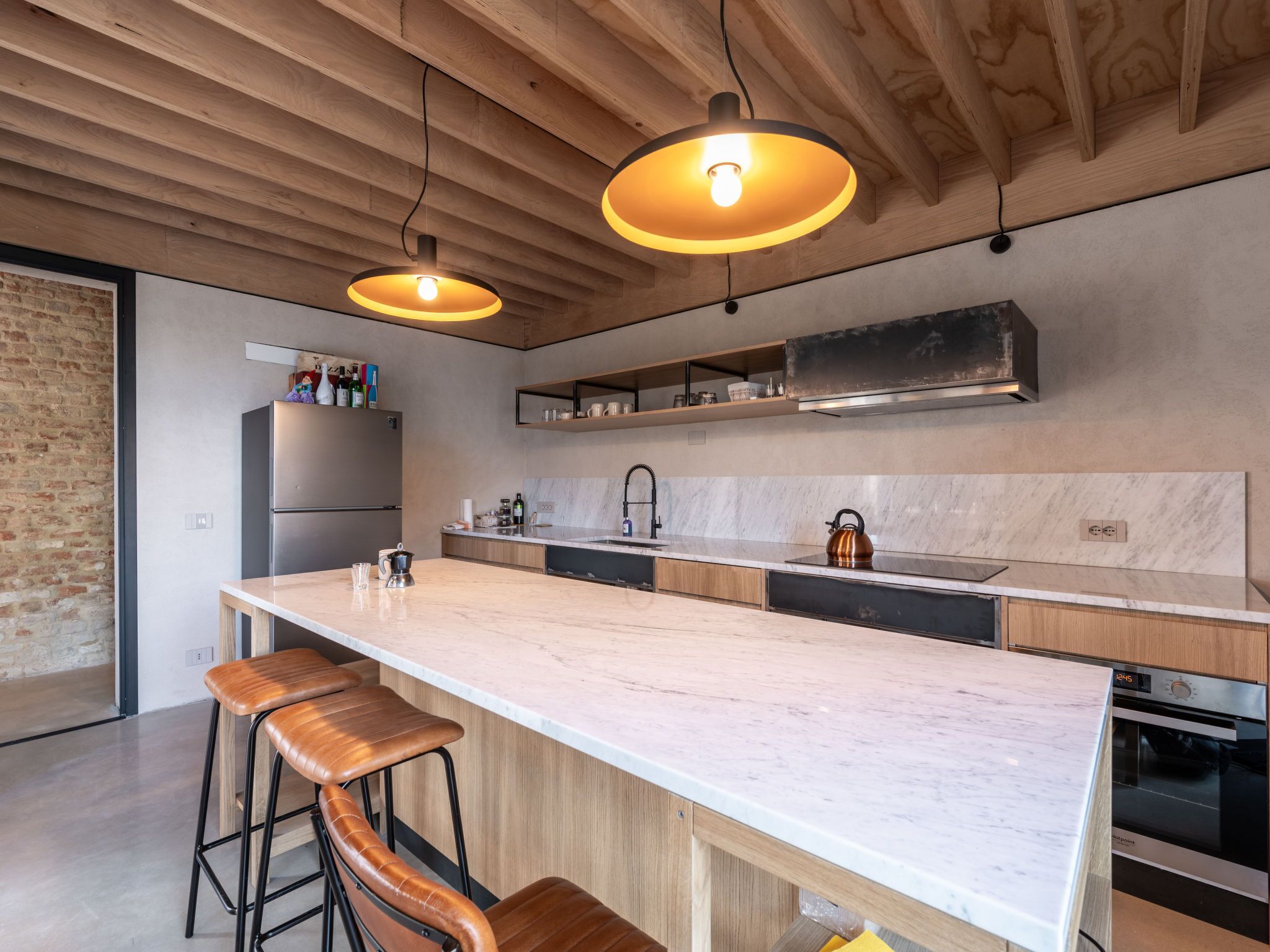 Een moderne keuken met een groot eiland, barstoelen, een roestvrijstalen koelkast en een inbouwoven.