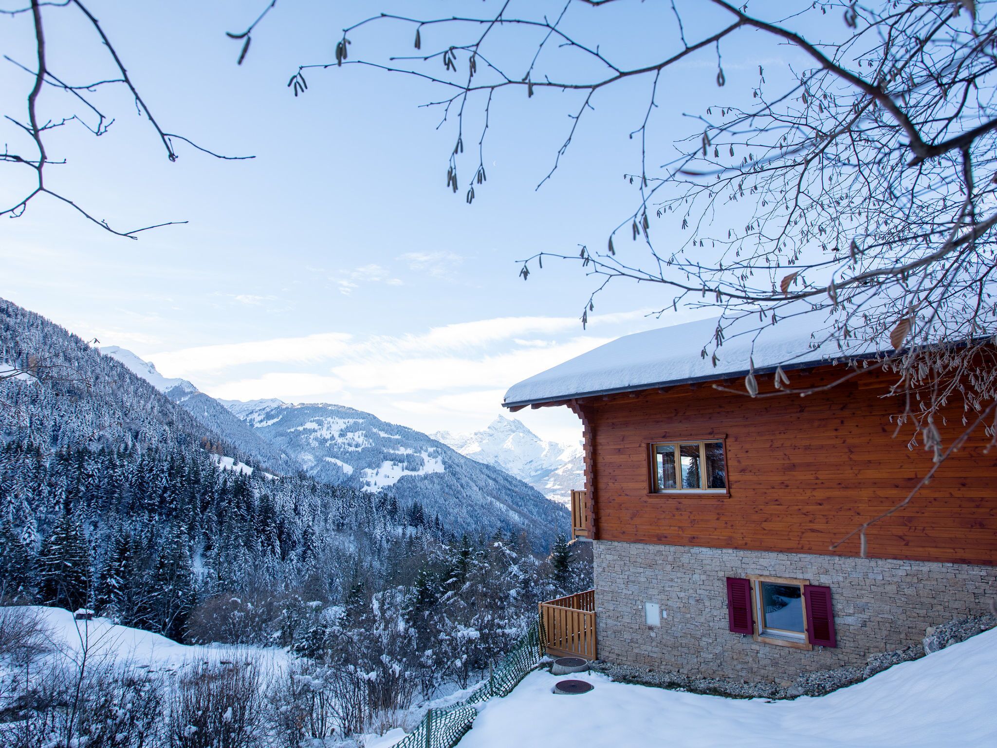Eine Holzhütte mit verschneitem Dach, umgeben von schneebedeckten Bäumen und Bergen.