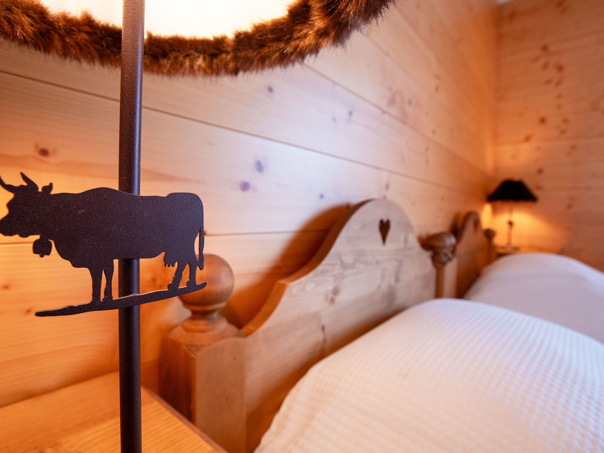Een houten blokhut van binnen, met een bed, een decoratie van een koeien silhouet en een lamp.