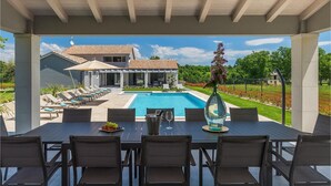 An outdoor pool area with a covered patio, lounge chairs, and a dining table with chairs.