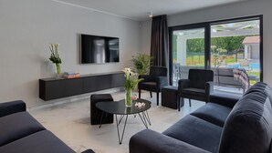 A modern living room with a flat-screen TV, a sofa set, a coffee table, and a view of a swimming pool.