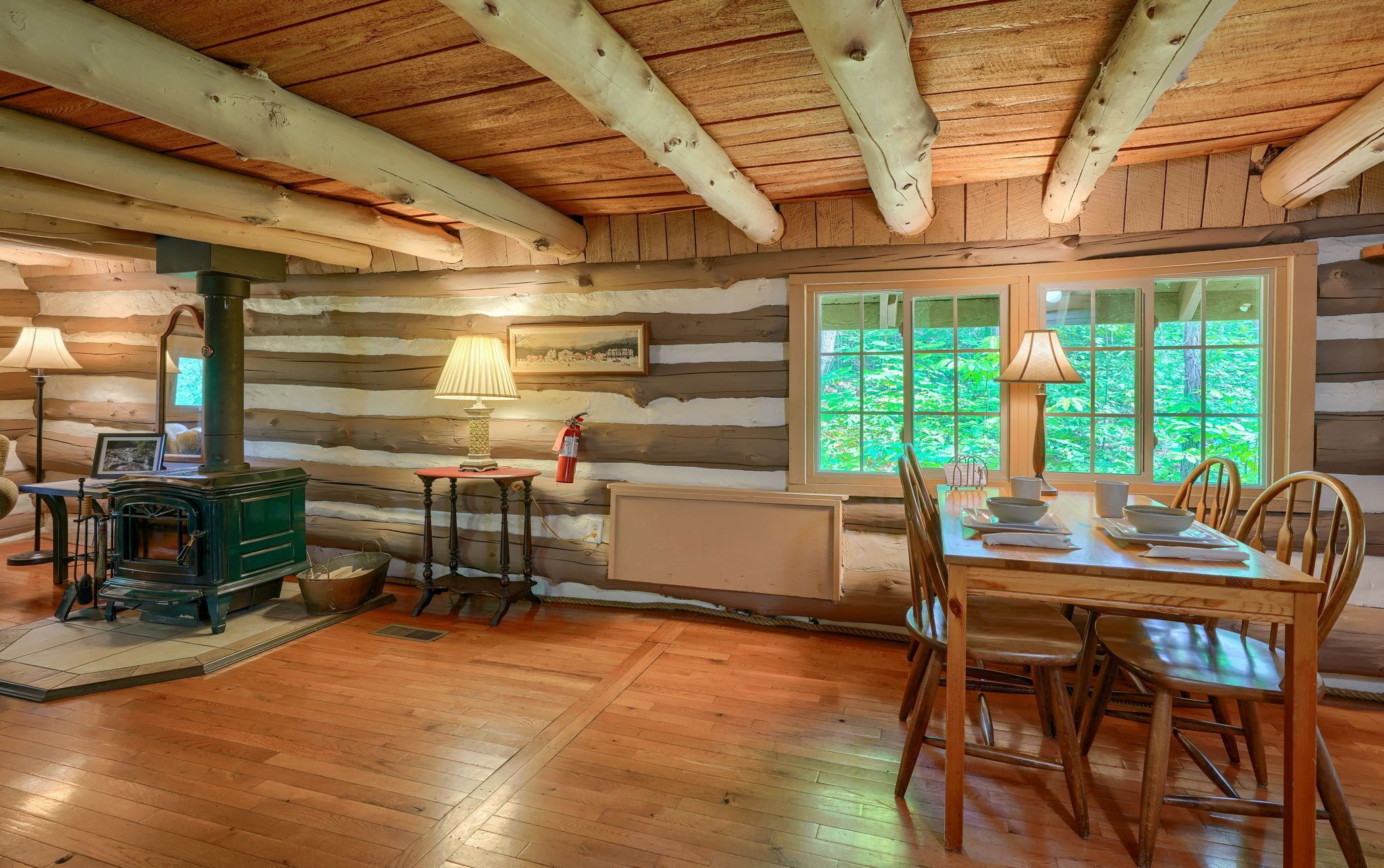 Ein rustikales Blockhaus-Interieur mit Essbereich, Holzwänden, einem Herd und großen Fenstern.