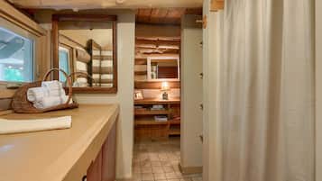 Een badkamer met een houten wastafelmeubel, een spiegel, een handdoekhouder, een plank met toiletartikelen en een douchegordijn.