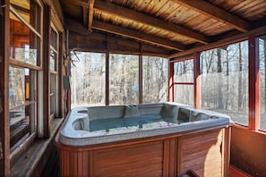 Eine Holzhütte mit Whirlpool, großen Fenstern und Blick auf einen Wald.