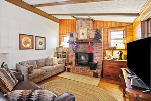 A cozy living room with a fireplace, a sofa, a television, and framed pictures on the wall.