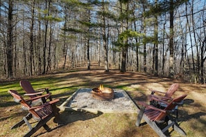 Ein Campingplatz mit zwei Adirondack-Stühlen um eine Feuerstelle, umgeben von einem Wald.